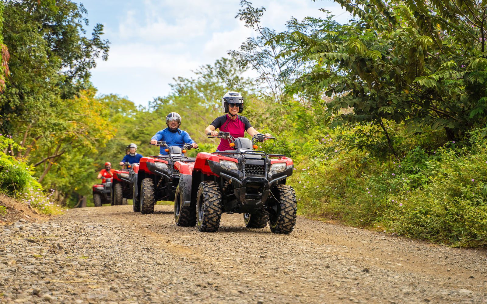 ATV riders on a rocky road surrounded by tropical greenery