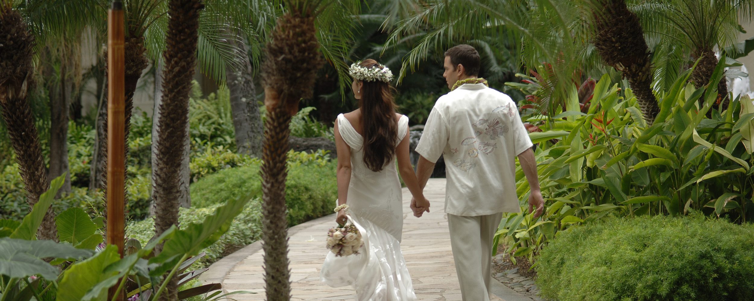 Wedding couple holding hands with backs faced and walking through the greenery of Hilton Hawaiian Village