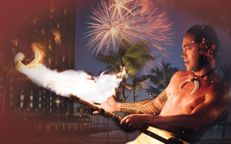 Waikiki Starlight Luau fire knife dancer holding large flame with fireworks from the resort's Friday Night Fireworks in the background