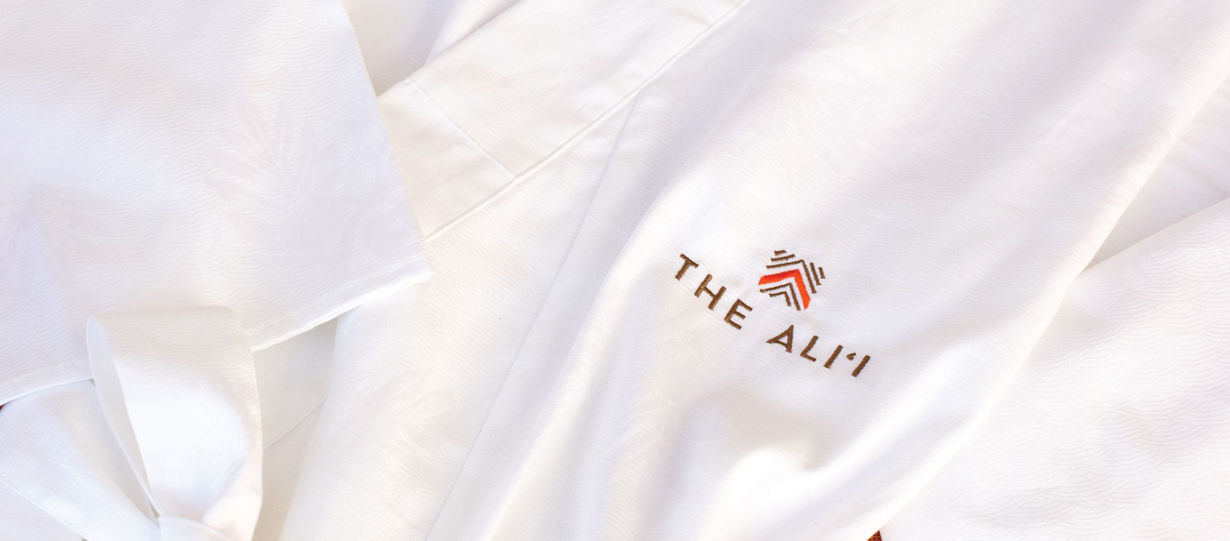 Embroidery of The Alii logo on a crisp white robe folded