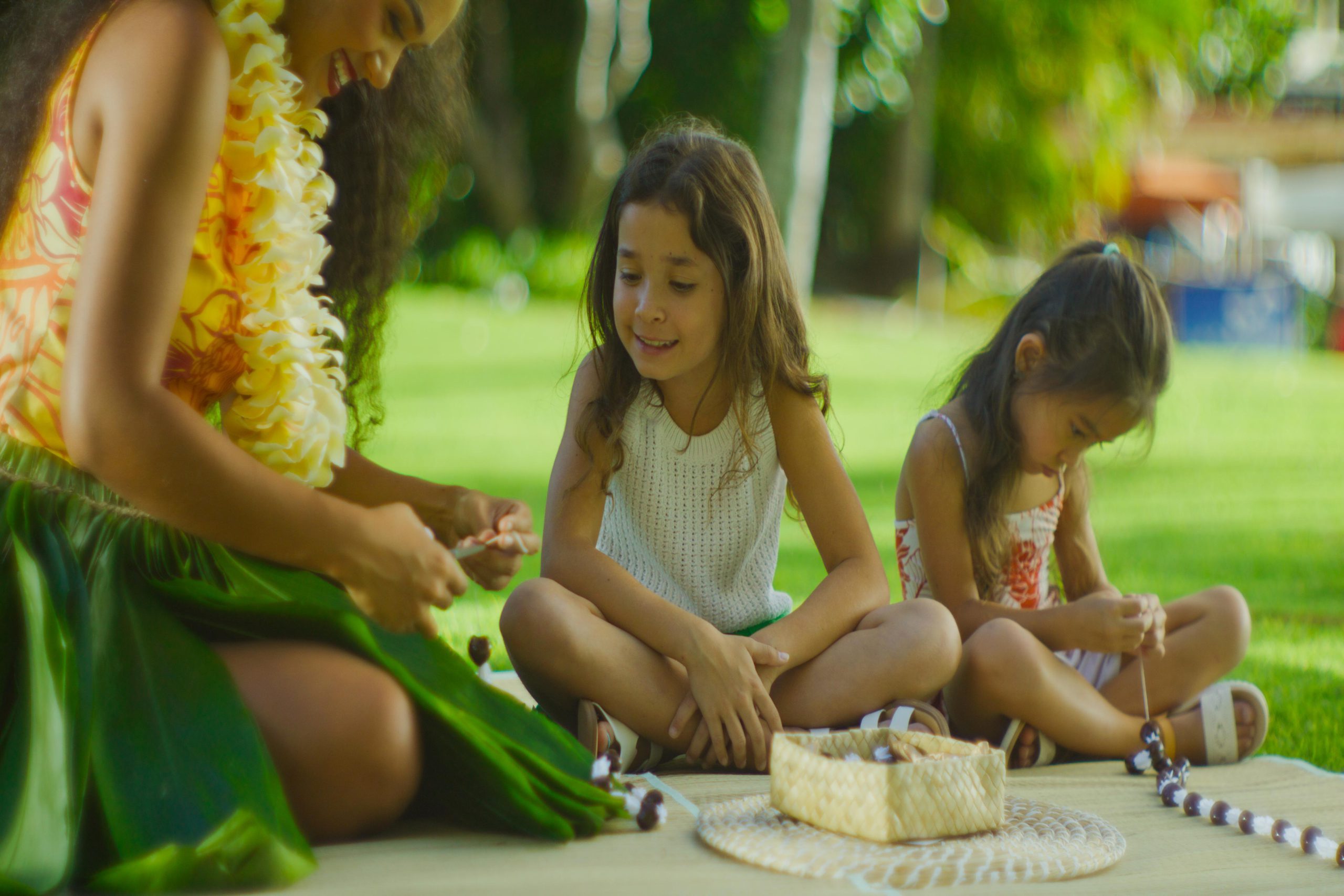 Kids making a kukui nut lei with an instructor