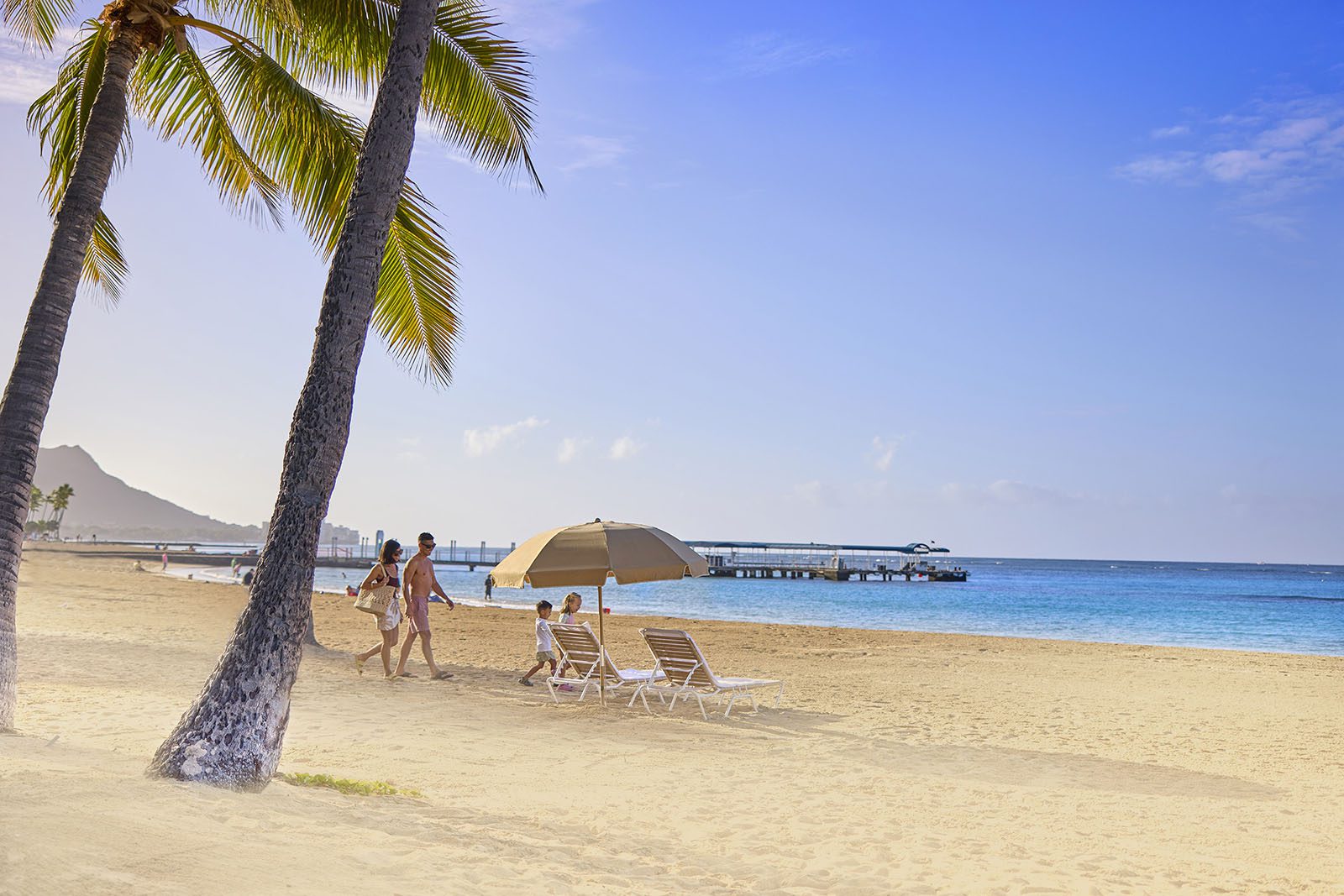 Couple with children strolling to their beach umbrella on Waikiki Beach