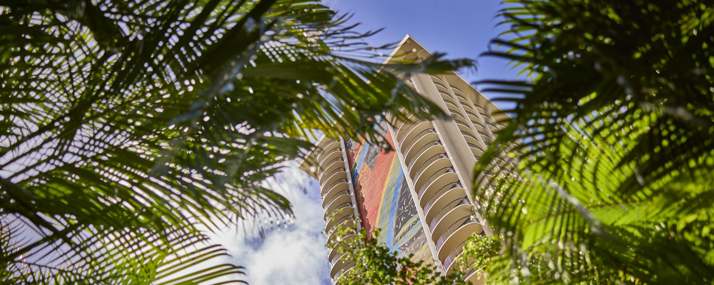 A view of Rainbow Tower looking up to the tower's rainbow mosaic through palm leaves